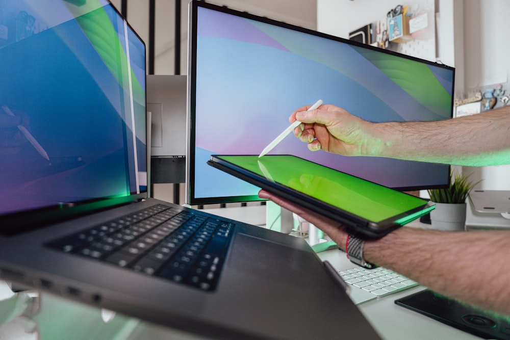 a man is holding a laptop in front of a computer screen