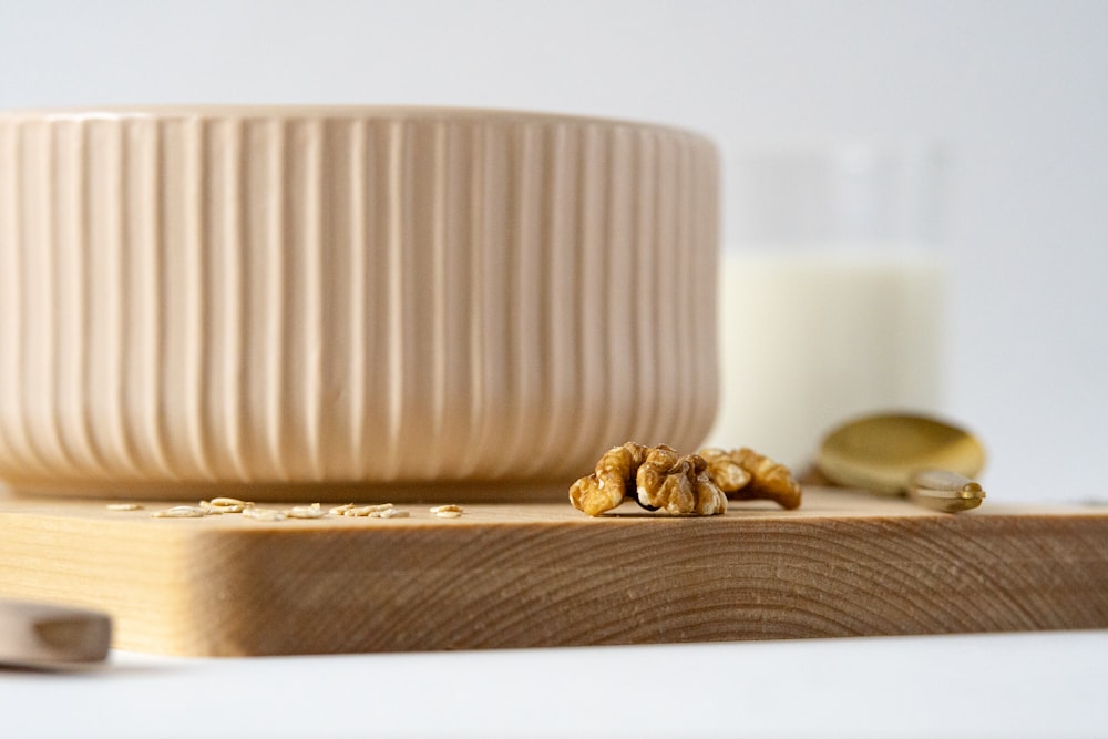a wooden cutting board topped with a bowl of nuts next to a glass of milk