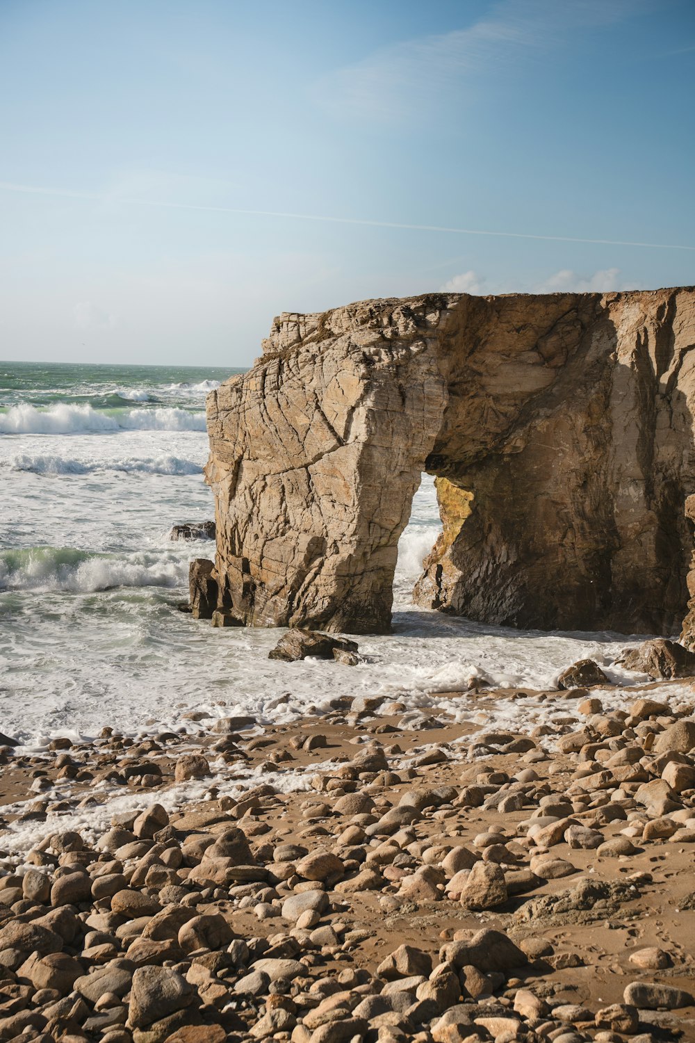a rocky beach with a large rock arch in the middle of it