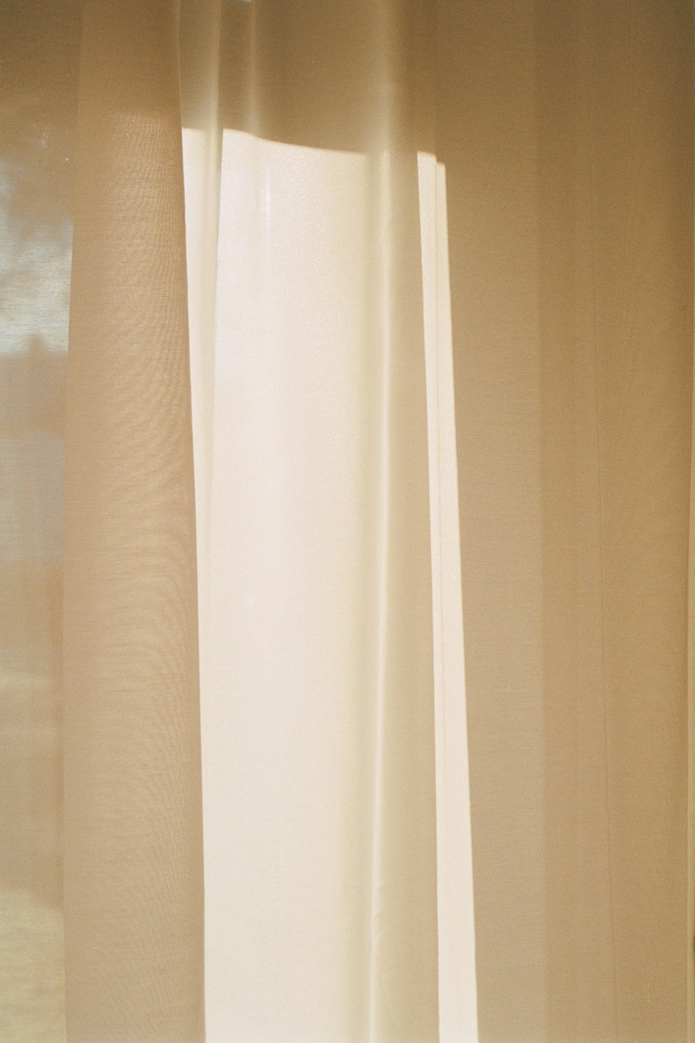 a window with a white curtain and a cat sitting on the window sill