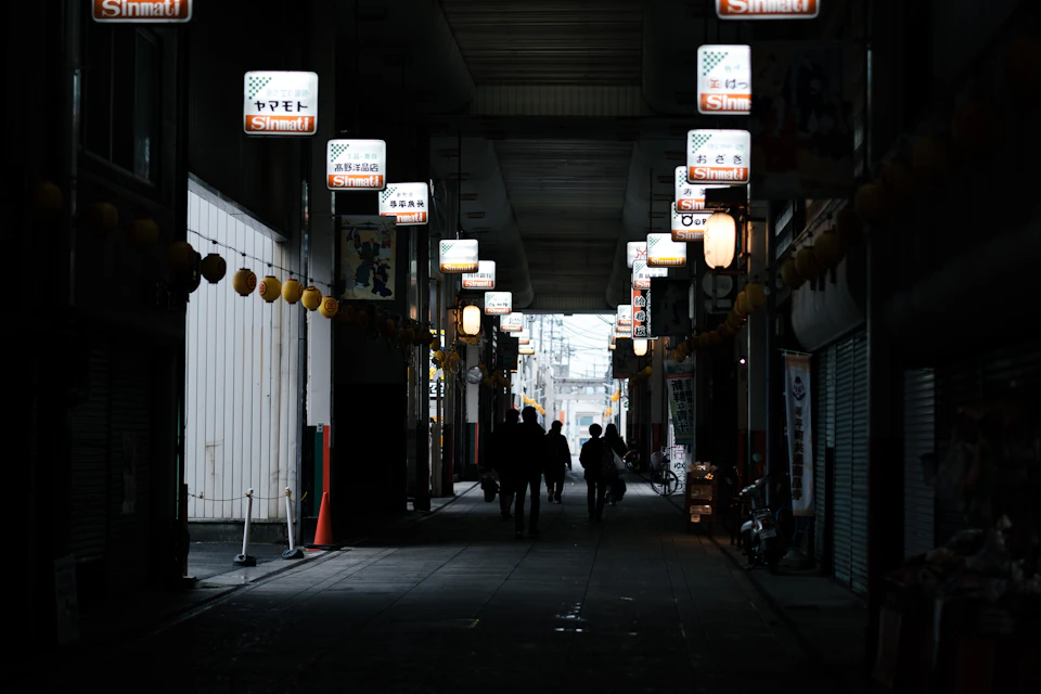 Three individuals walk down a narrow alleyway with silhouettes against colorful signs and lights