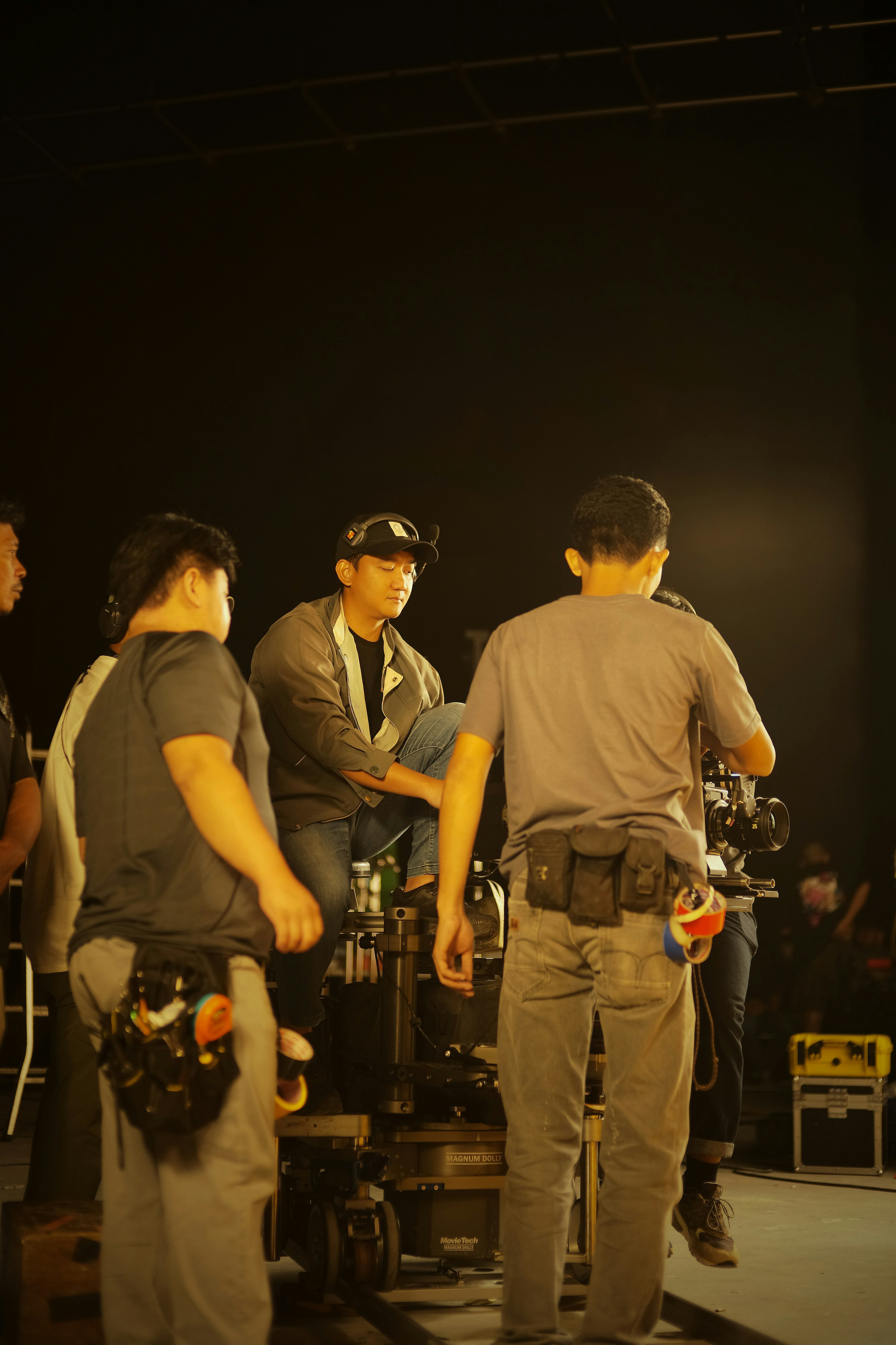 Film production set with professional lighting rigs, dark studio environment, cinematic equipment in background