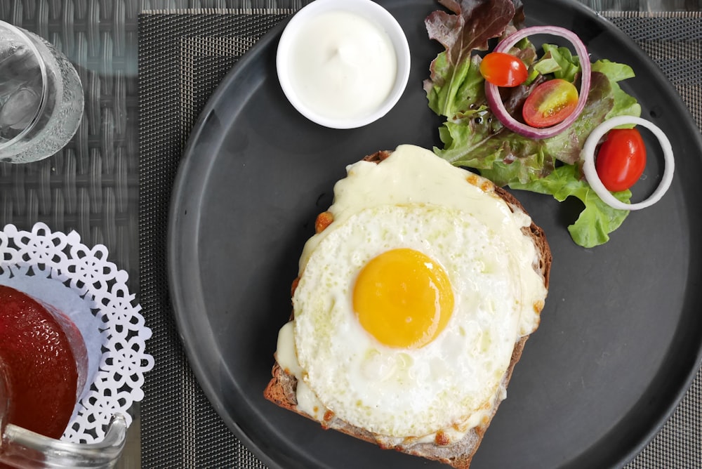 a black plate topped with a fried egg and a salad