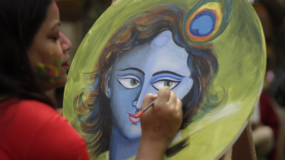 a woman holding a painting of a woman with a peacock on her head