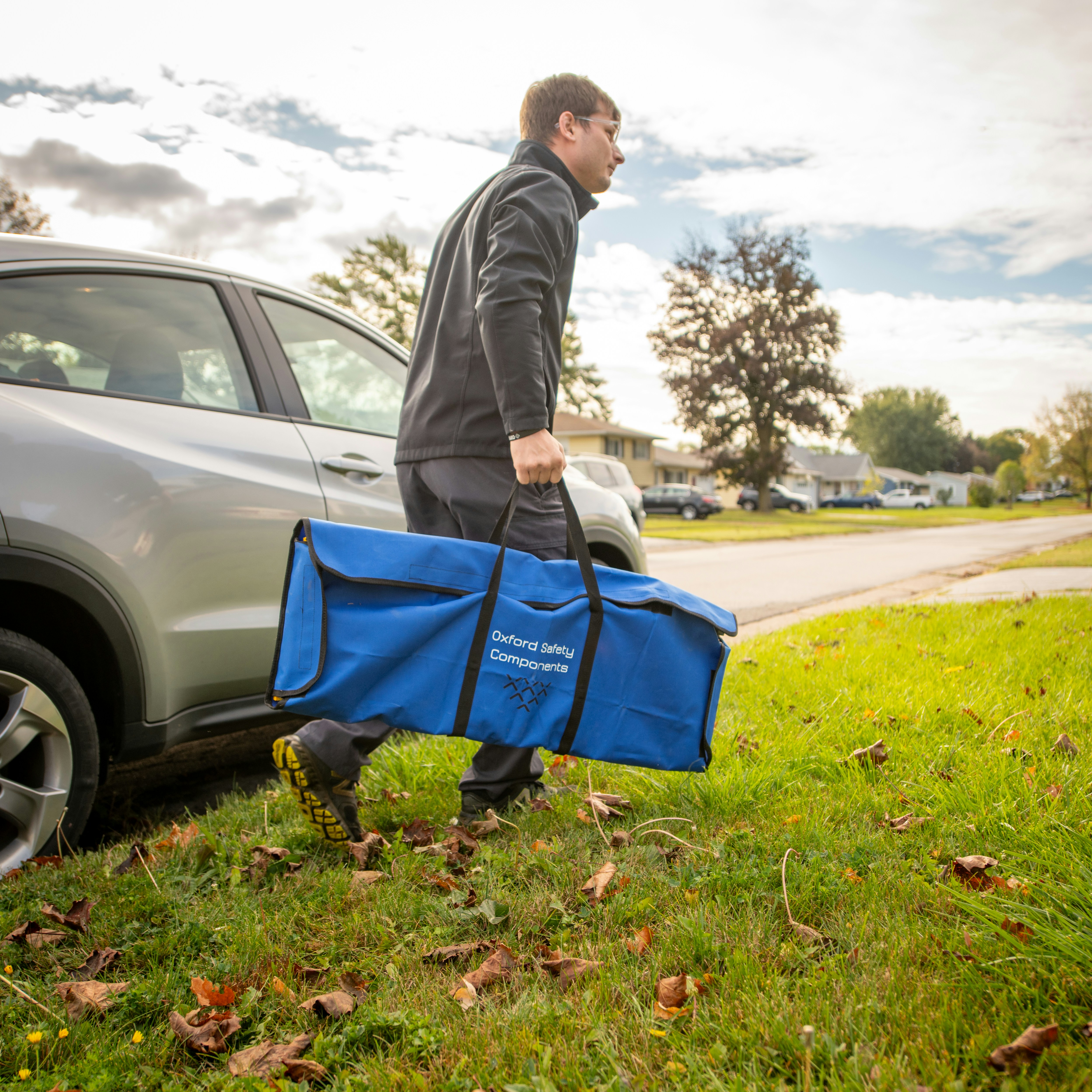 a man carrying a large blue bag next to a car
