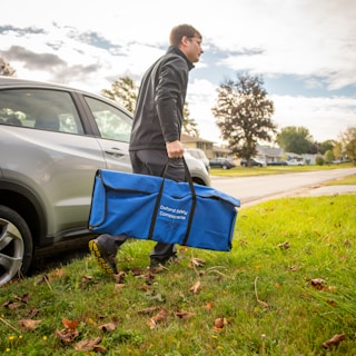 a man carrying a large blue bag next to a car