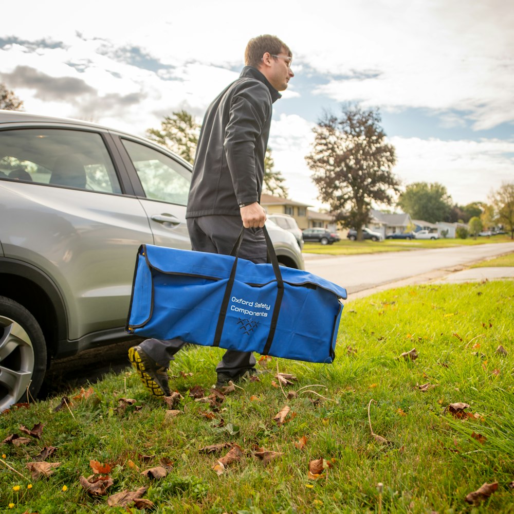 a man carrying a large blue bag next to a car