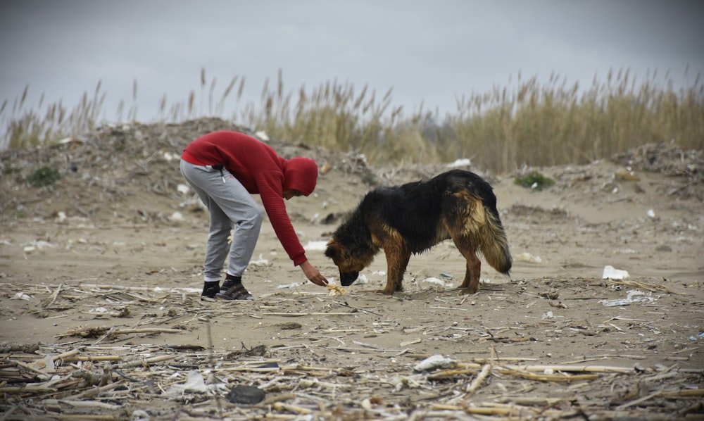 a man in a red hoodie petting a black and brown dog