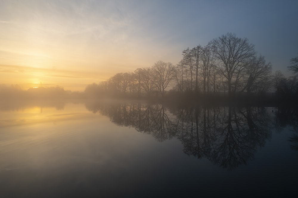 the sun is setting over a lake with trees in the background