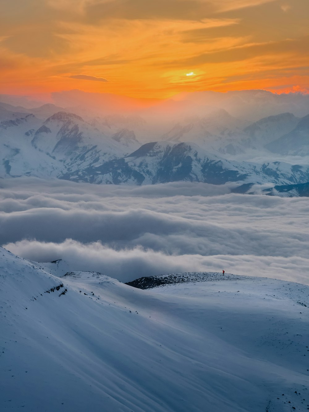 the sun is setting over the mountains covered in clouds