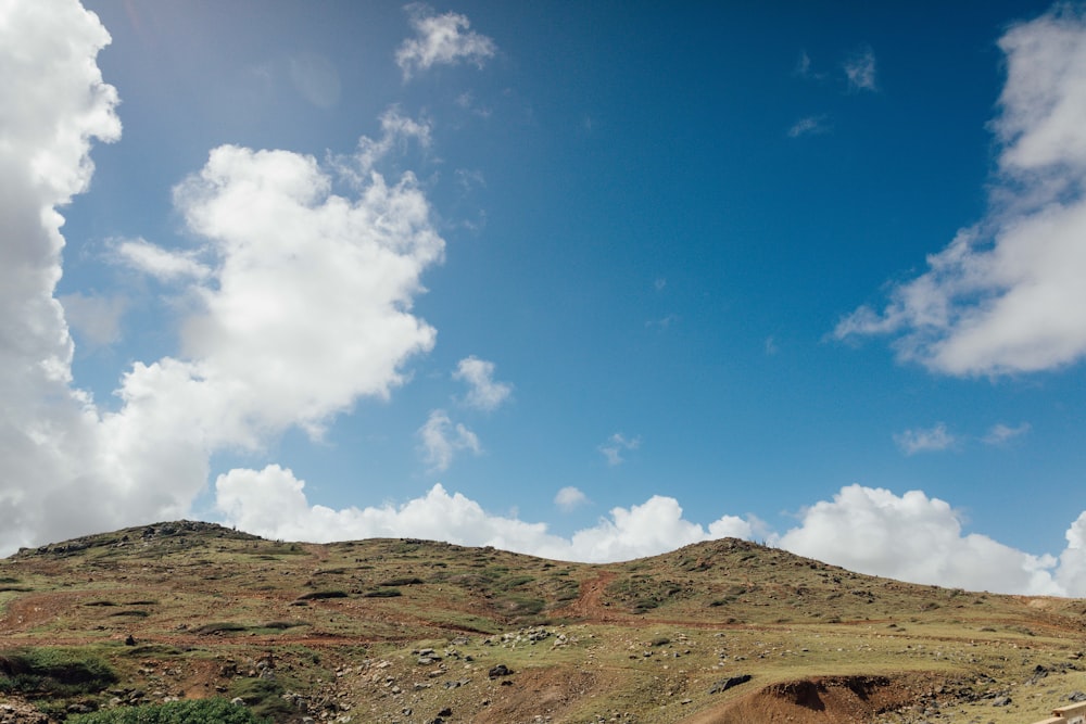 a dirt road going up a hill under a cloudy blue sky