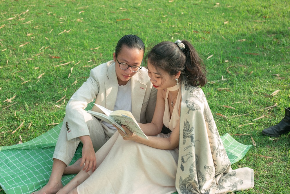 a man and woman sitting on a blanket reading a book