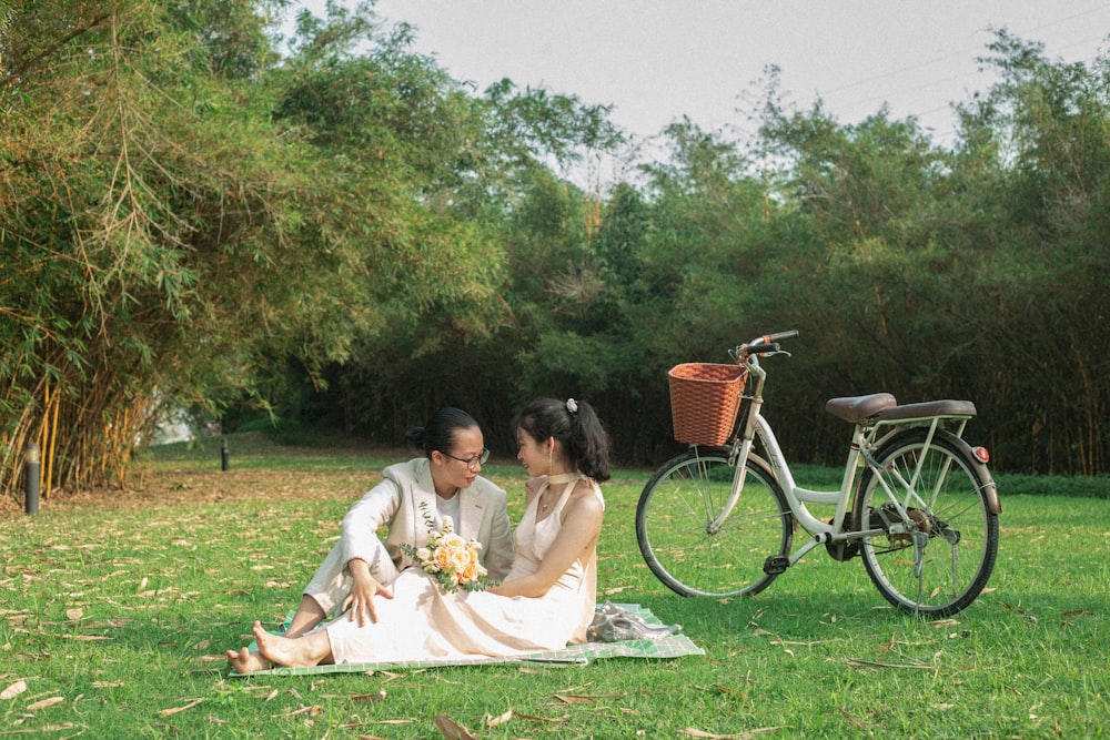 a man and a woman sitting on a blanket in a field next to a bike