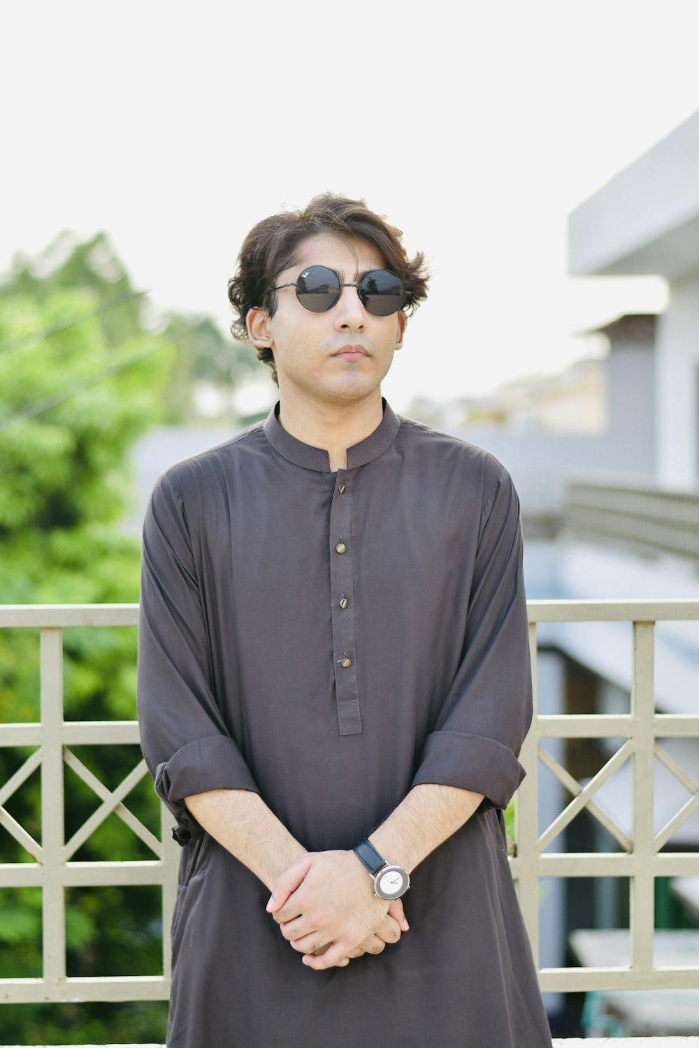 a man wearing sunglasses standing in front of a fence