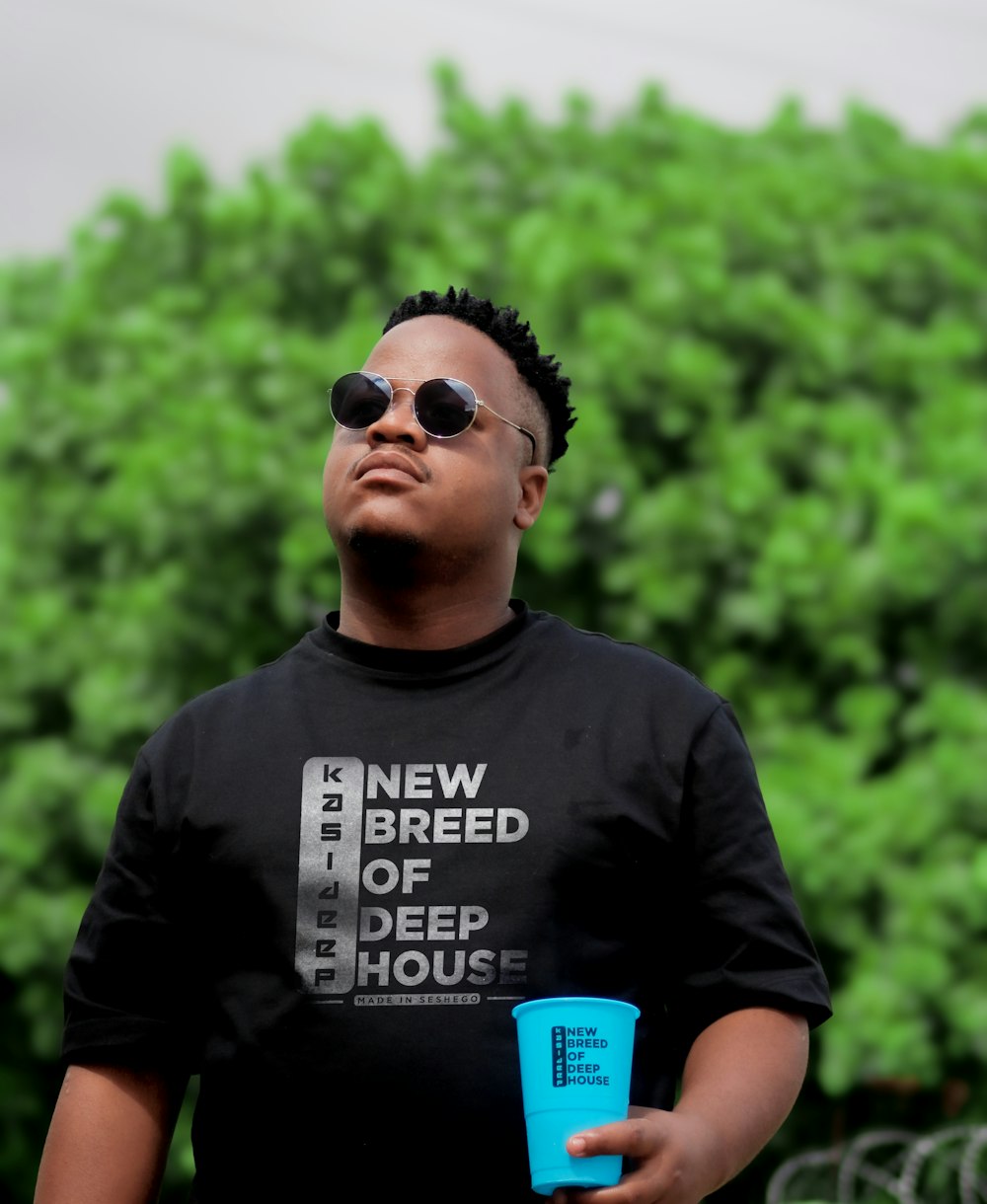 a man wearing a new breed of deep house t - shirt holding a blue cup