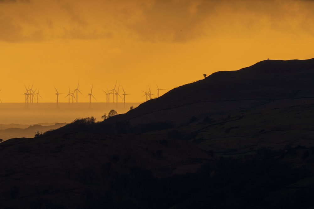 a group of windmills on a hill at sunset
