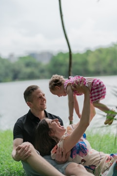 a man, woman and child are sitting on the grass by the water