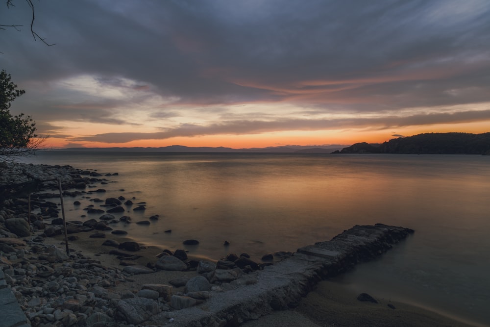a sunset over a body of water with rocks on the shore