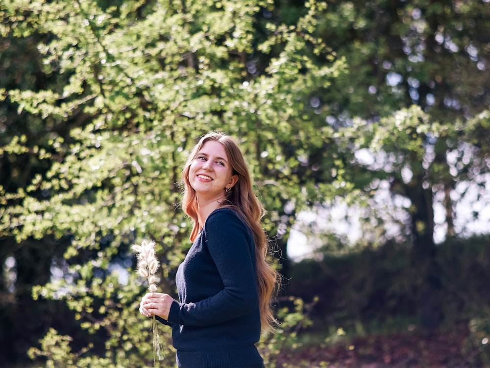 a woman standing in front of a tree holding a dandelion