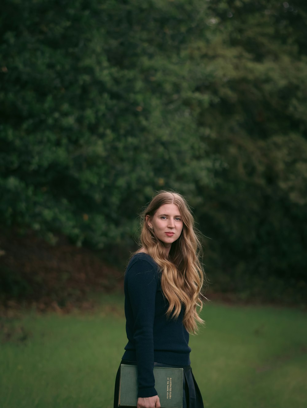 a woman standing in a field holding a book