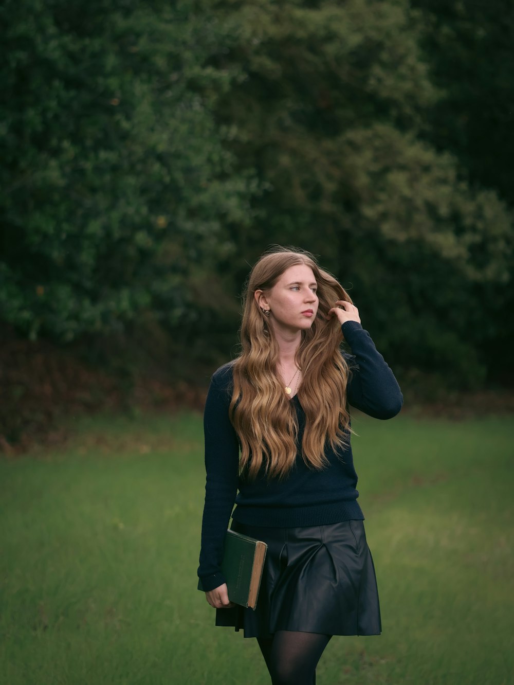 a woman walking in a field with a book in her hand