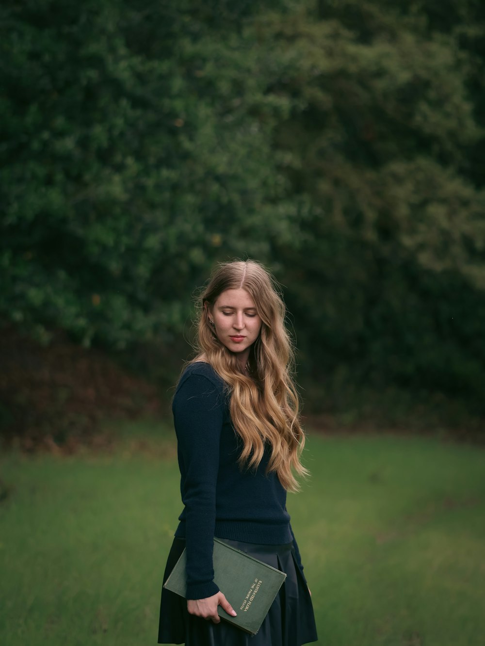 a woman standing in a field holding a book