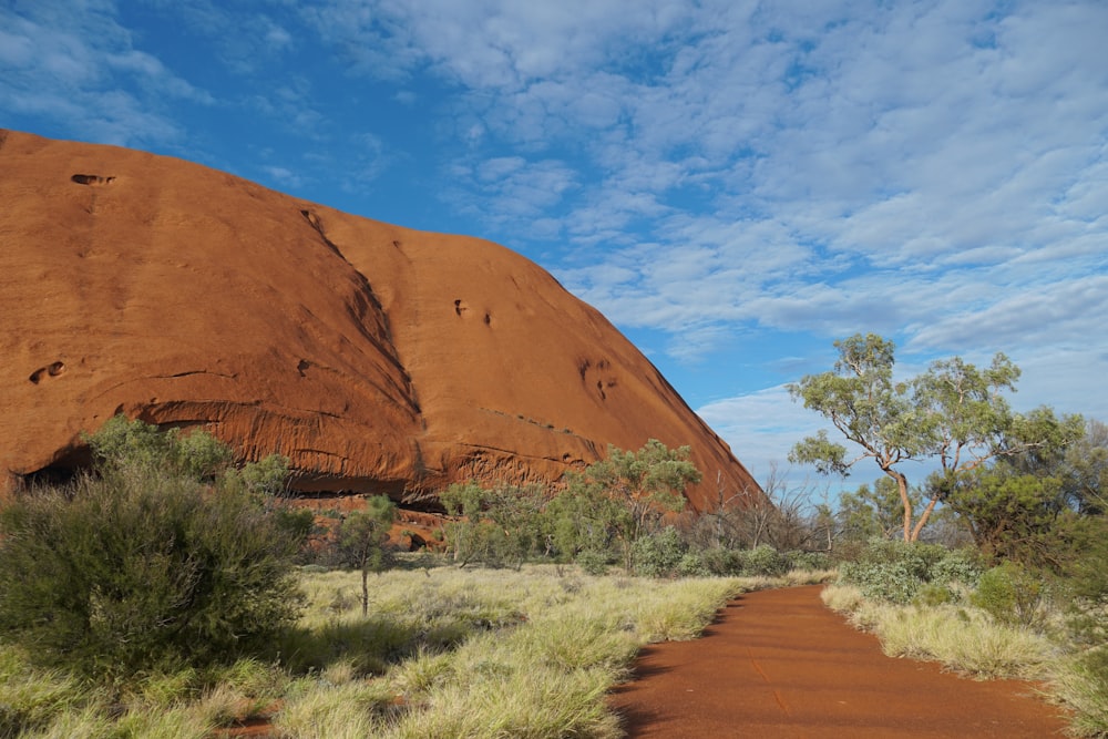 a dirt road in front of a large rock