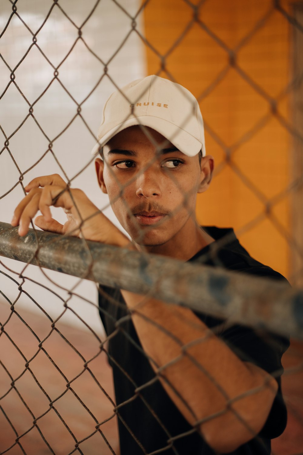 a man leaning against a fence with a baseball cap on