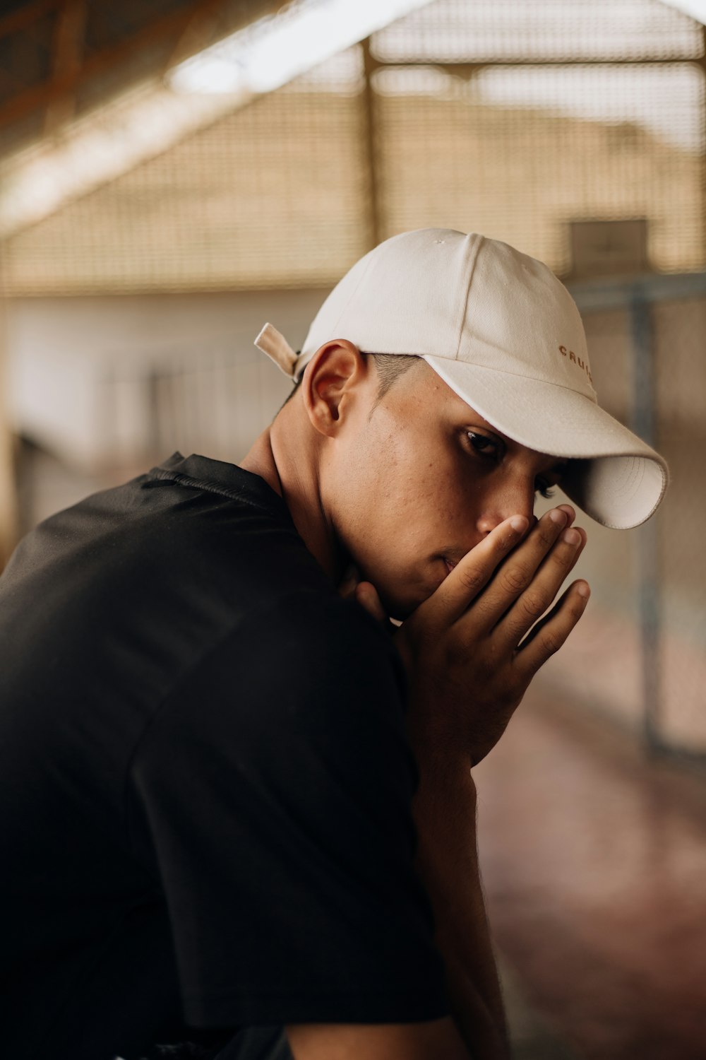 a man wearing a hat covers his face with his hands