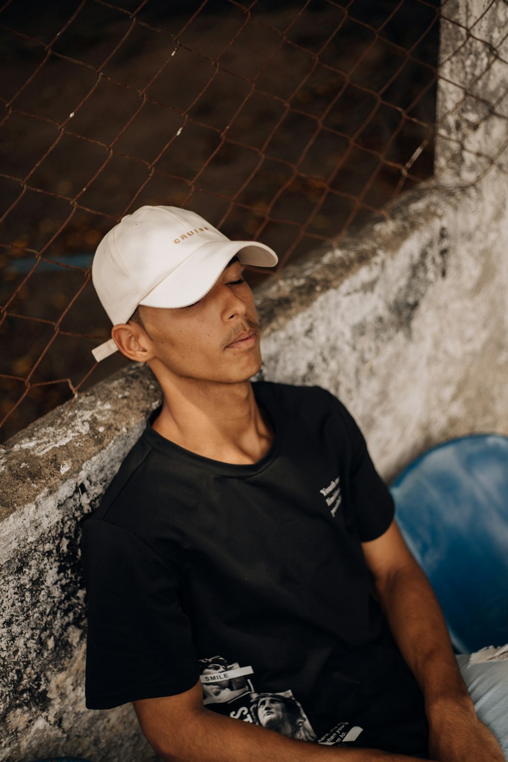 a man wearing a white hat sitting next to a fence