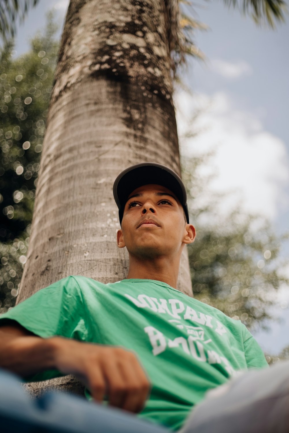 a man in a green shirt sitting next to a palm tree