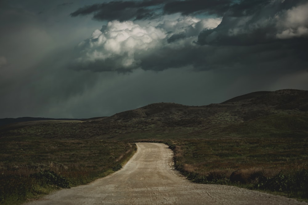 a dirt road in the middle of a field under a cloudy sky