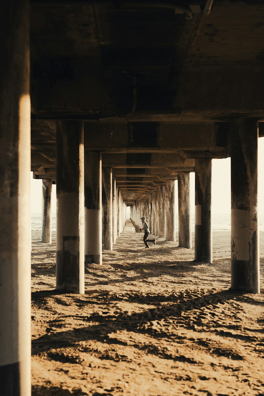 una persona parada debajo de un puente en una playa de arena