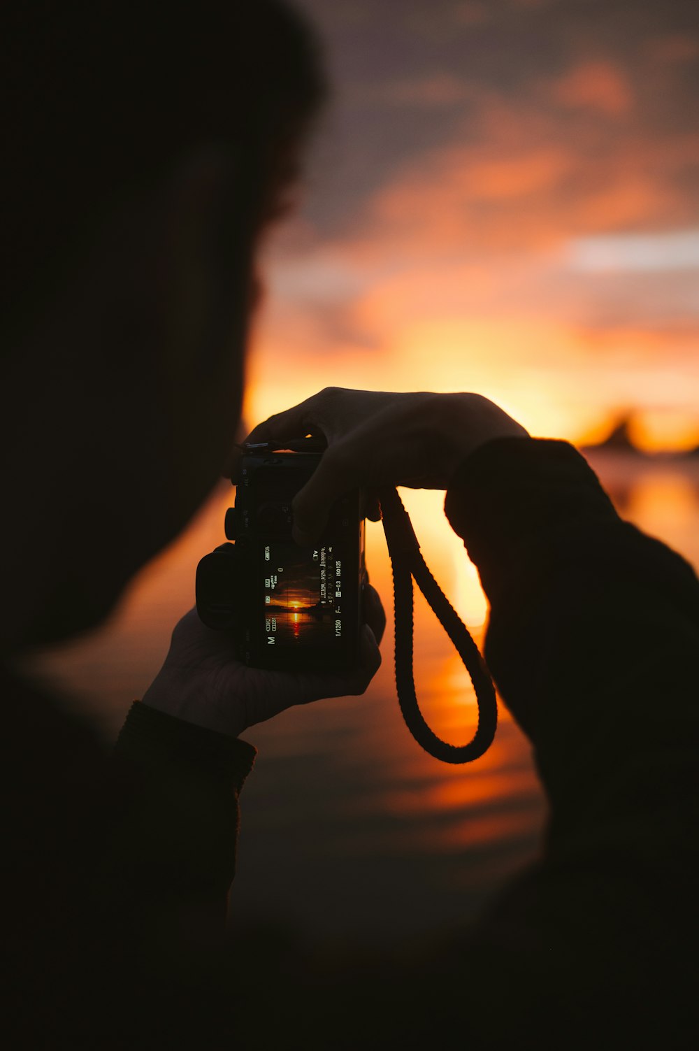 una persona tomando una foto de una puesta de sol con una cámara