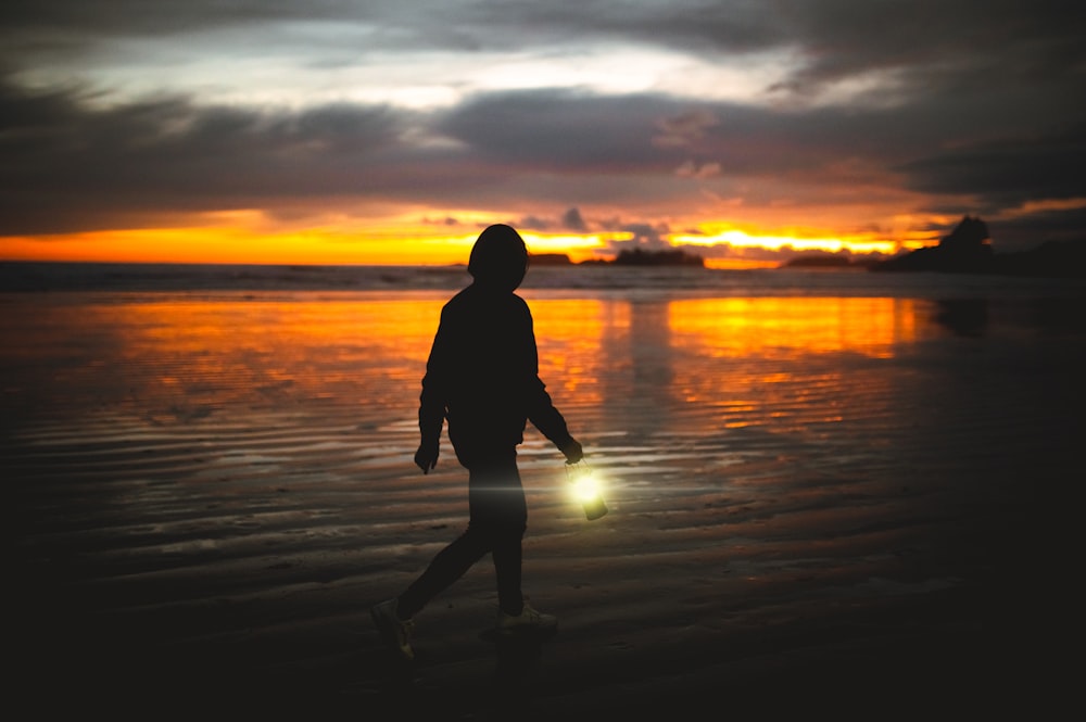 a person walking on a beach at sunset