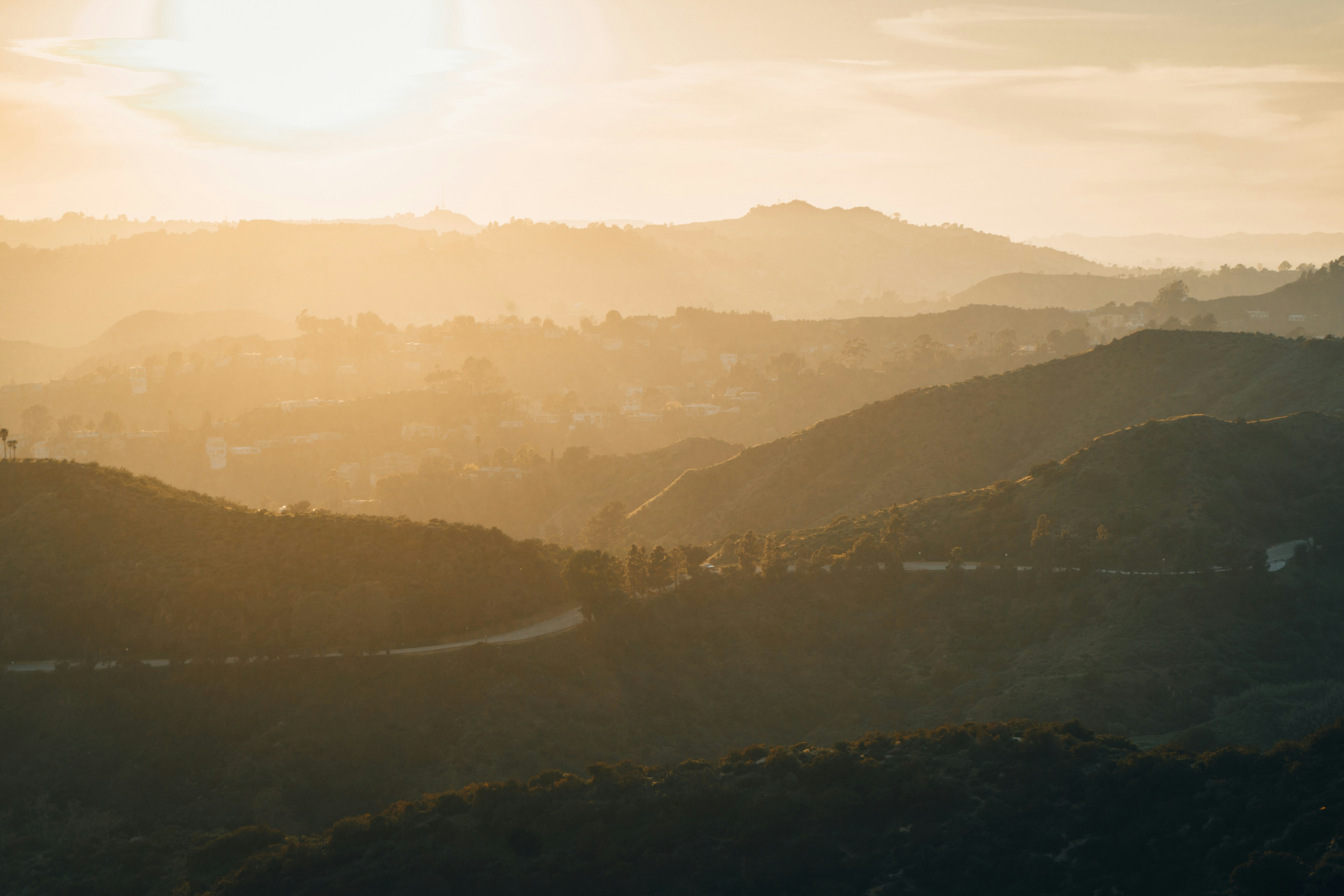 the sun is setting over the hills in the distance, 