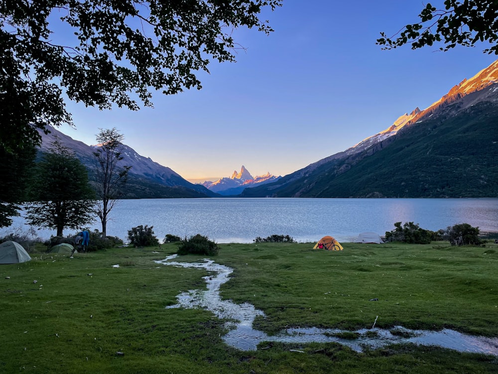 a tent set up on a grassy field next to a body of water