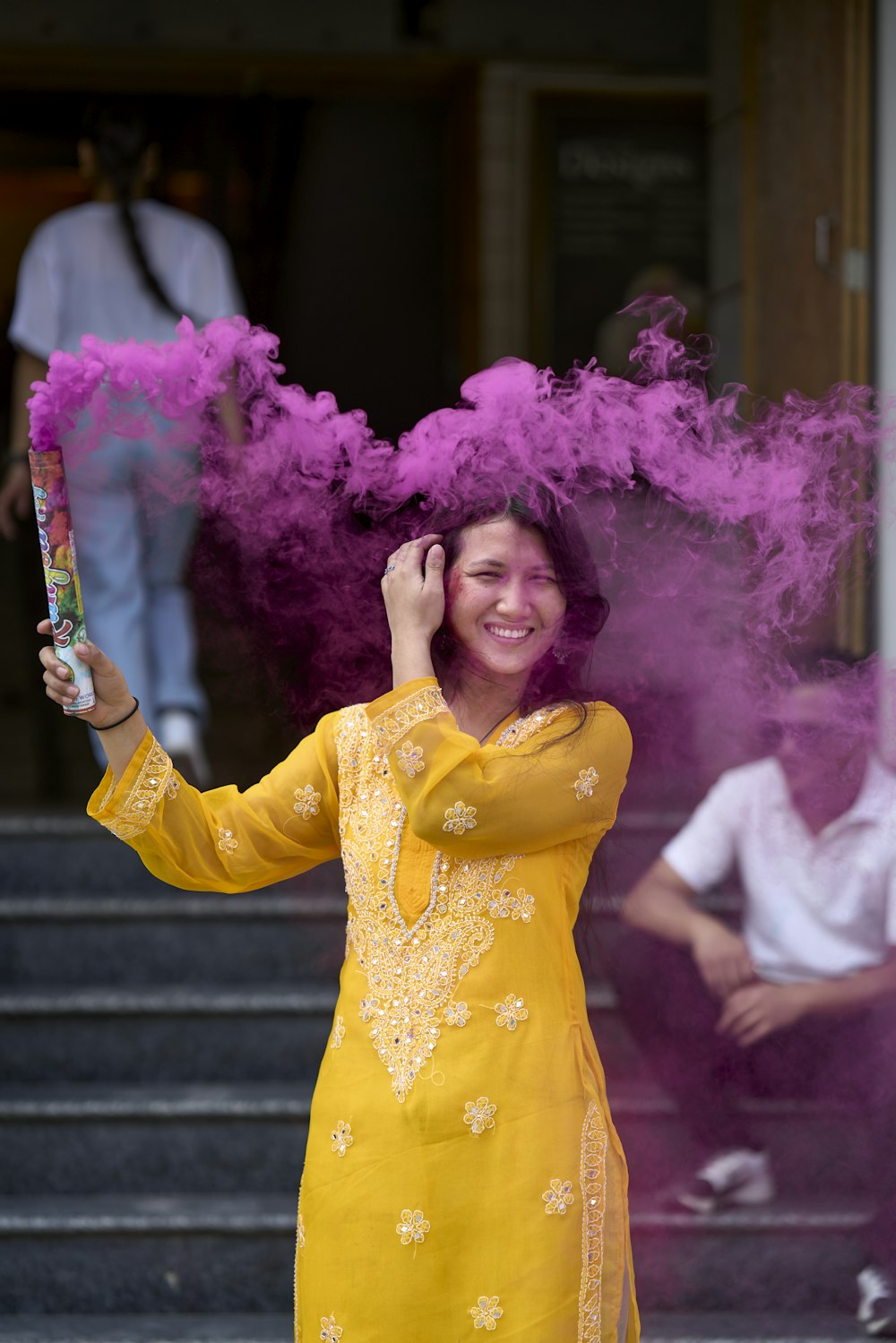 a woman in a yellow dress holding a pink smoke bomb