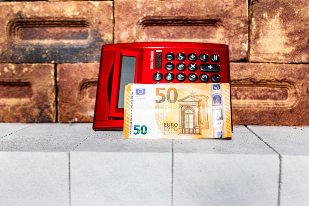 a red phone sitting on top of a counter next to a 50 euro bill