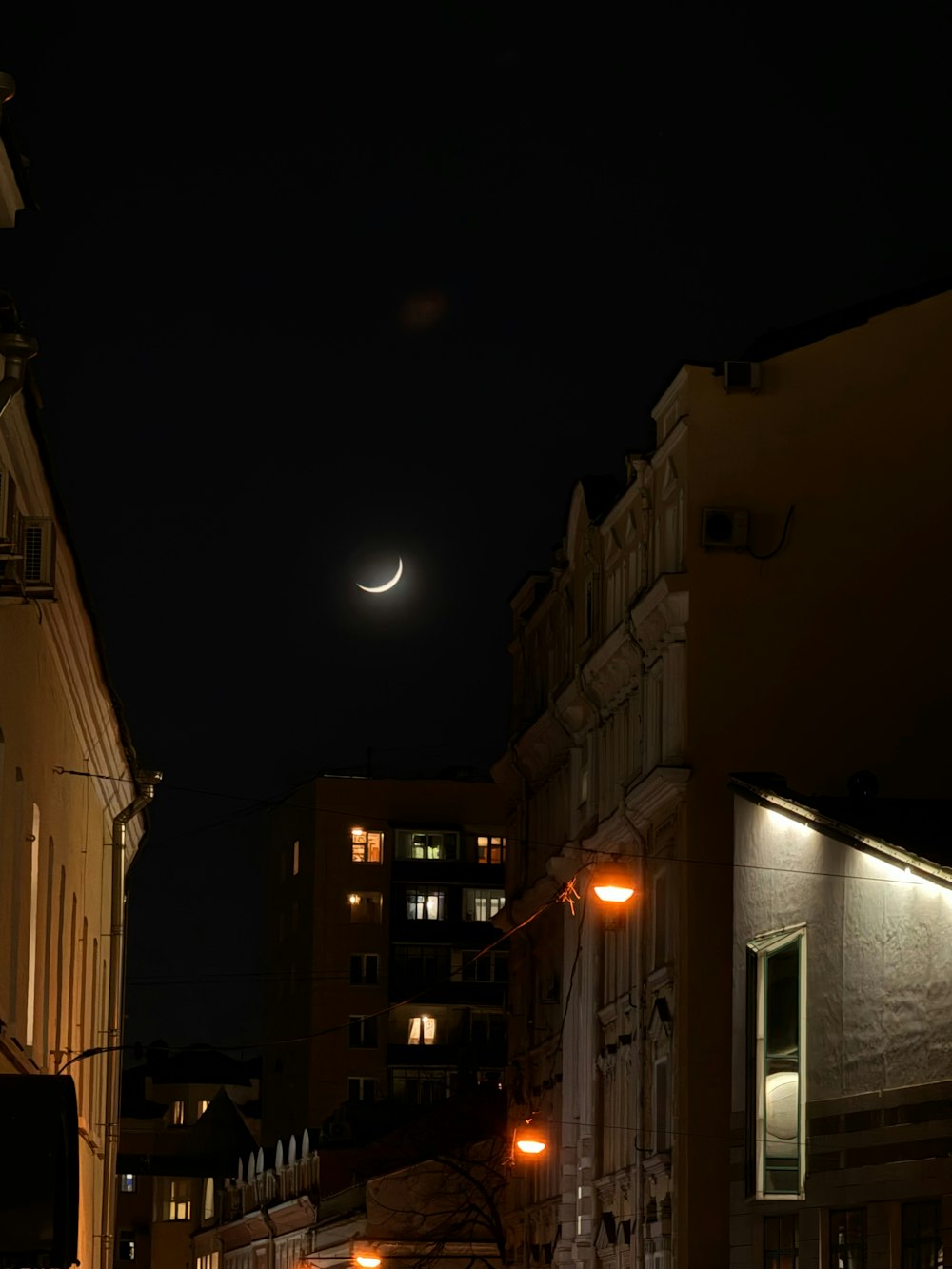 a street at night with a half moon in the sky