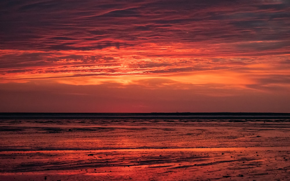 the sun is setting over the ocean with a boat in the distance