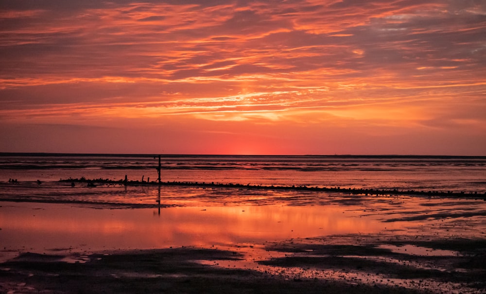 ein Sonnenuntergang über dem Meer mit einer Person, die am Strand spazieren geht