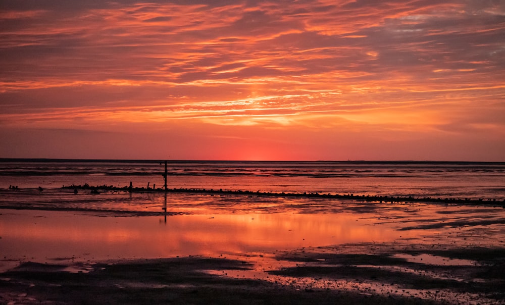 un coucher de soleil sur l’océan avec une personne marchant sur la plage