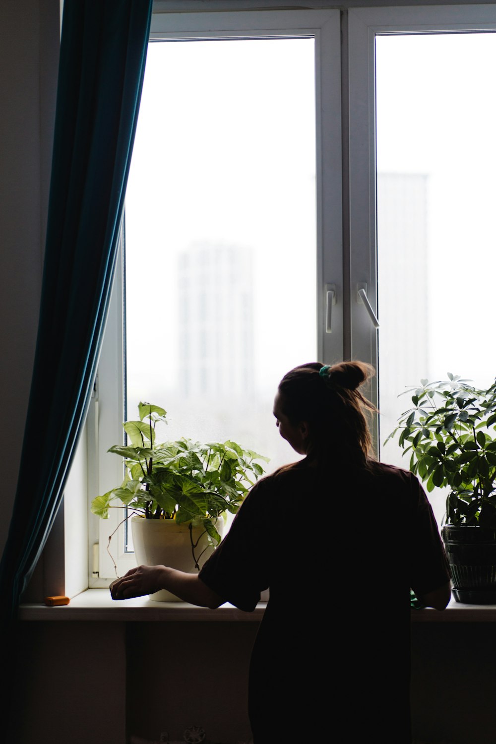 a woman standing in front of a window next to a potted plant