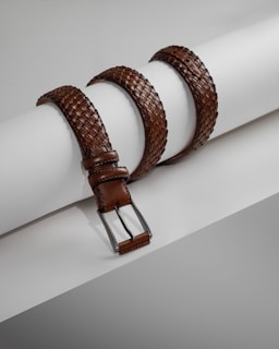 a pair of brown leather belts sitting on top of a white piece of paper