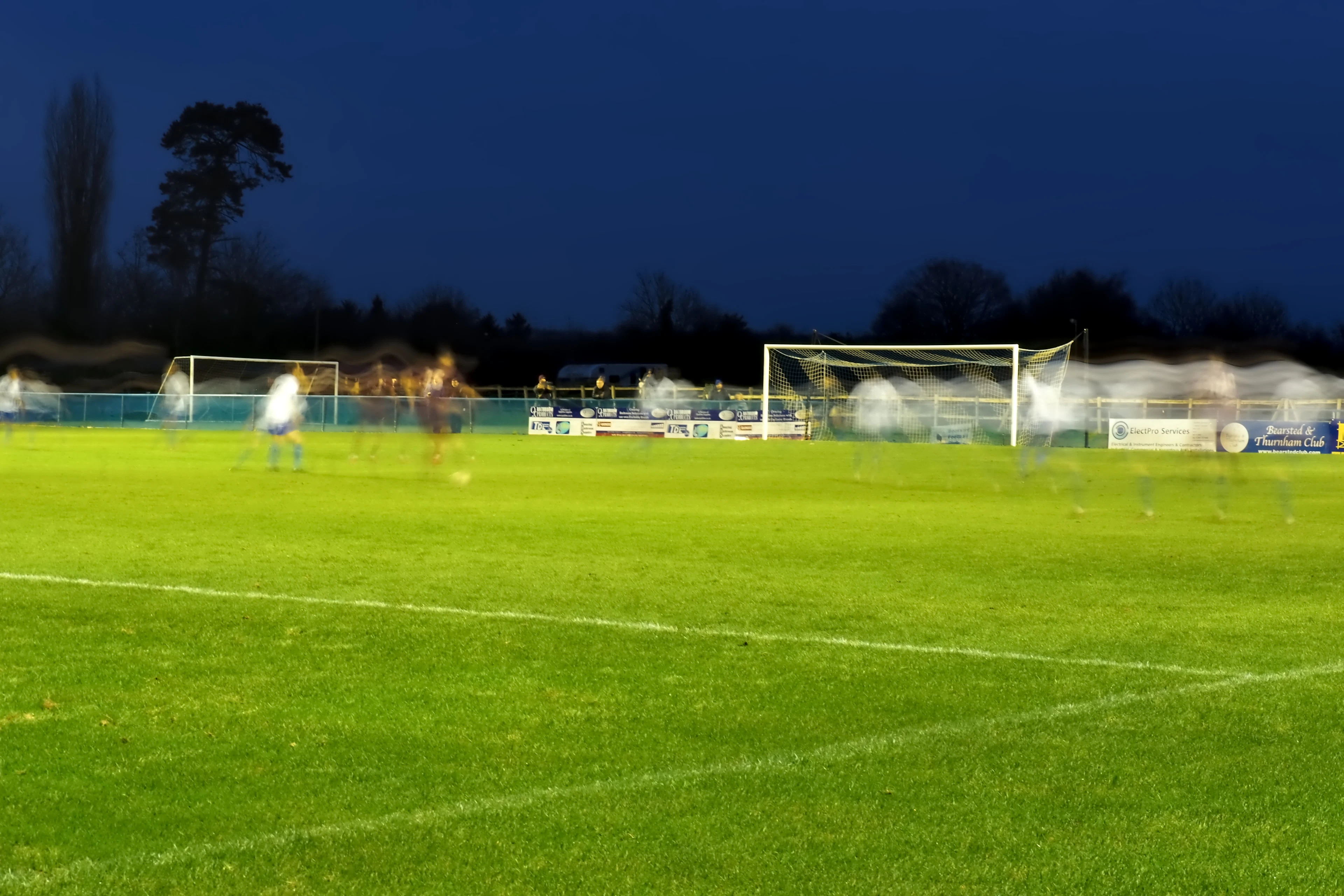 Teren de fotbal la apus, cu porți și stâlpi de nocturnă