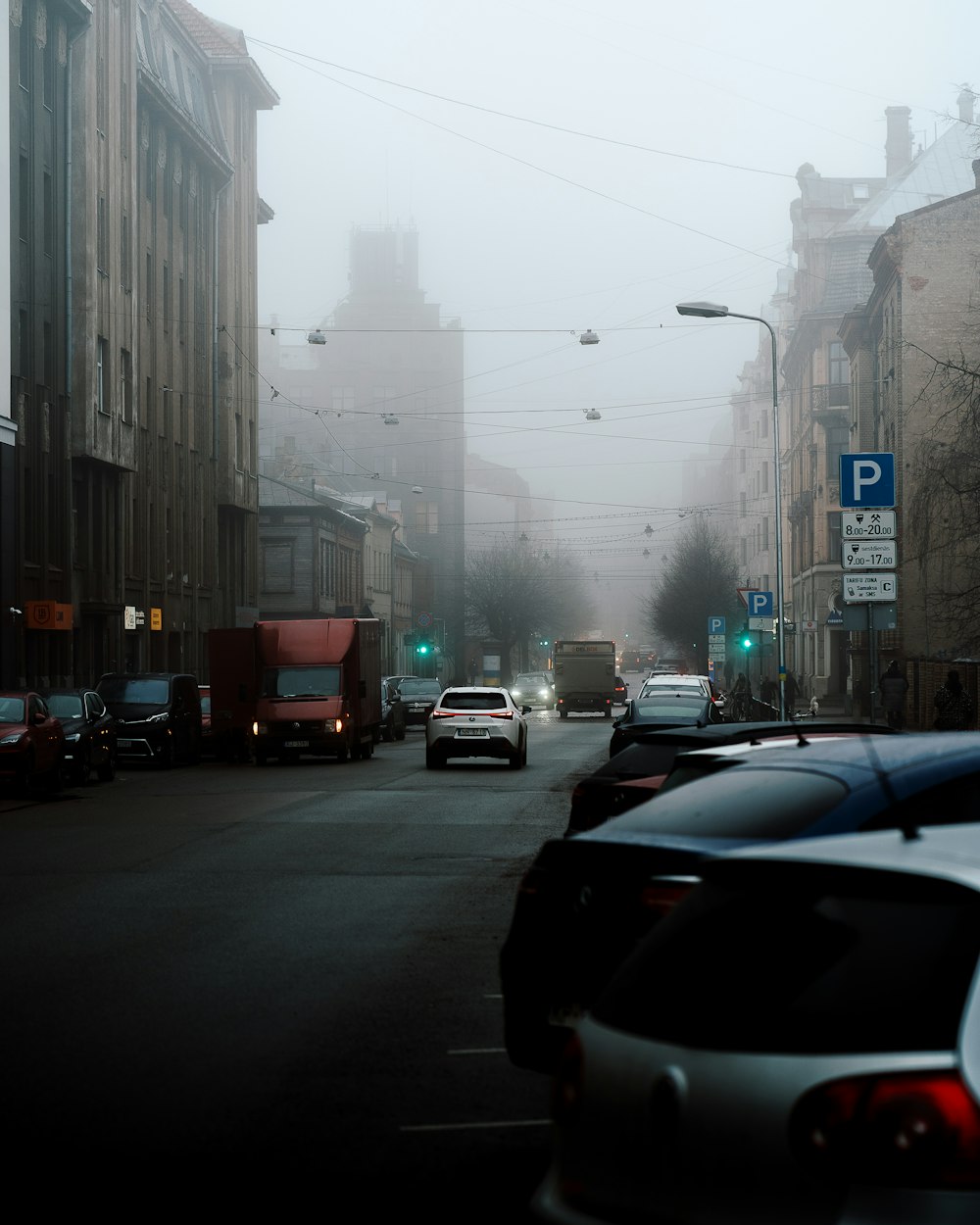 道路脇に車が停まっている霧の街の通り