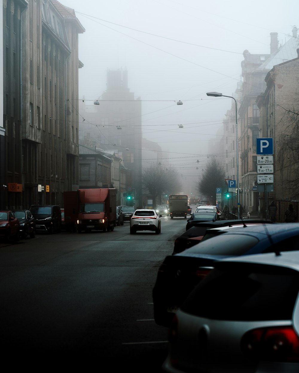 a foggy city street with cars parked on the side of the road