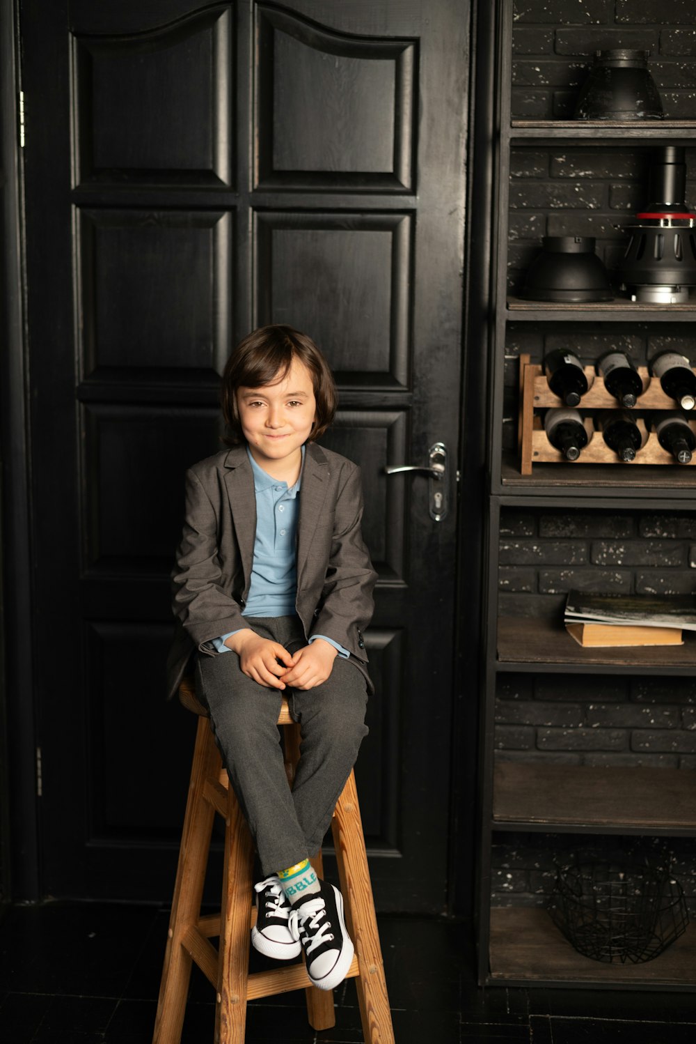 a young boy sitting on a stool in front of a black door