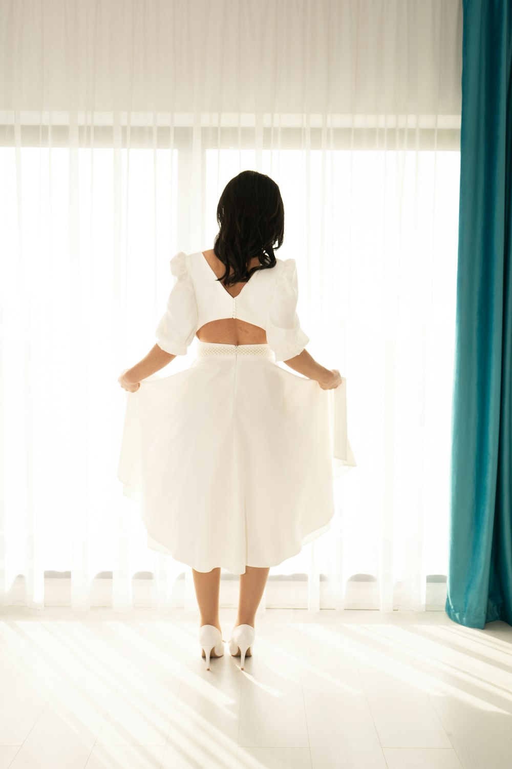 uma mulher com um vestido branco em pé em frente a uma janela